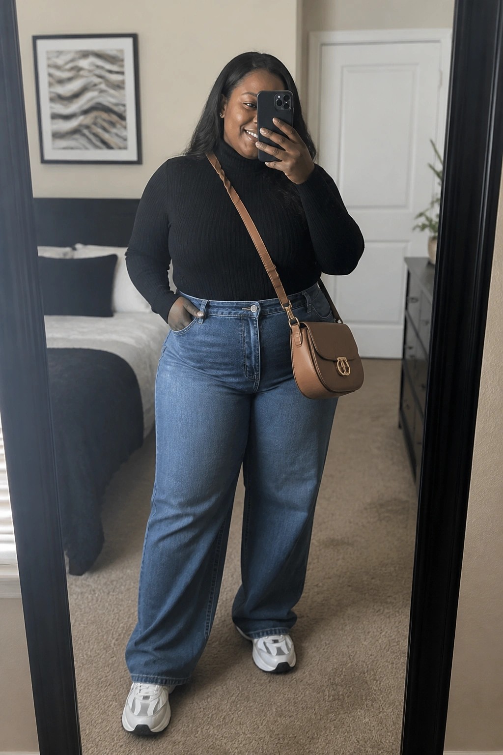 Woman in black turtleneck and blue jeans taking smiling mirror selfie with brown bag