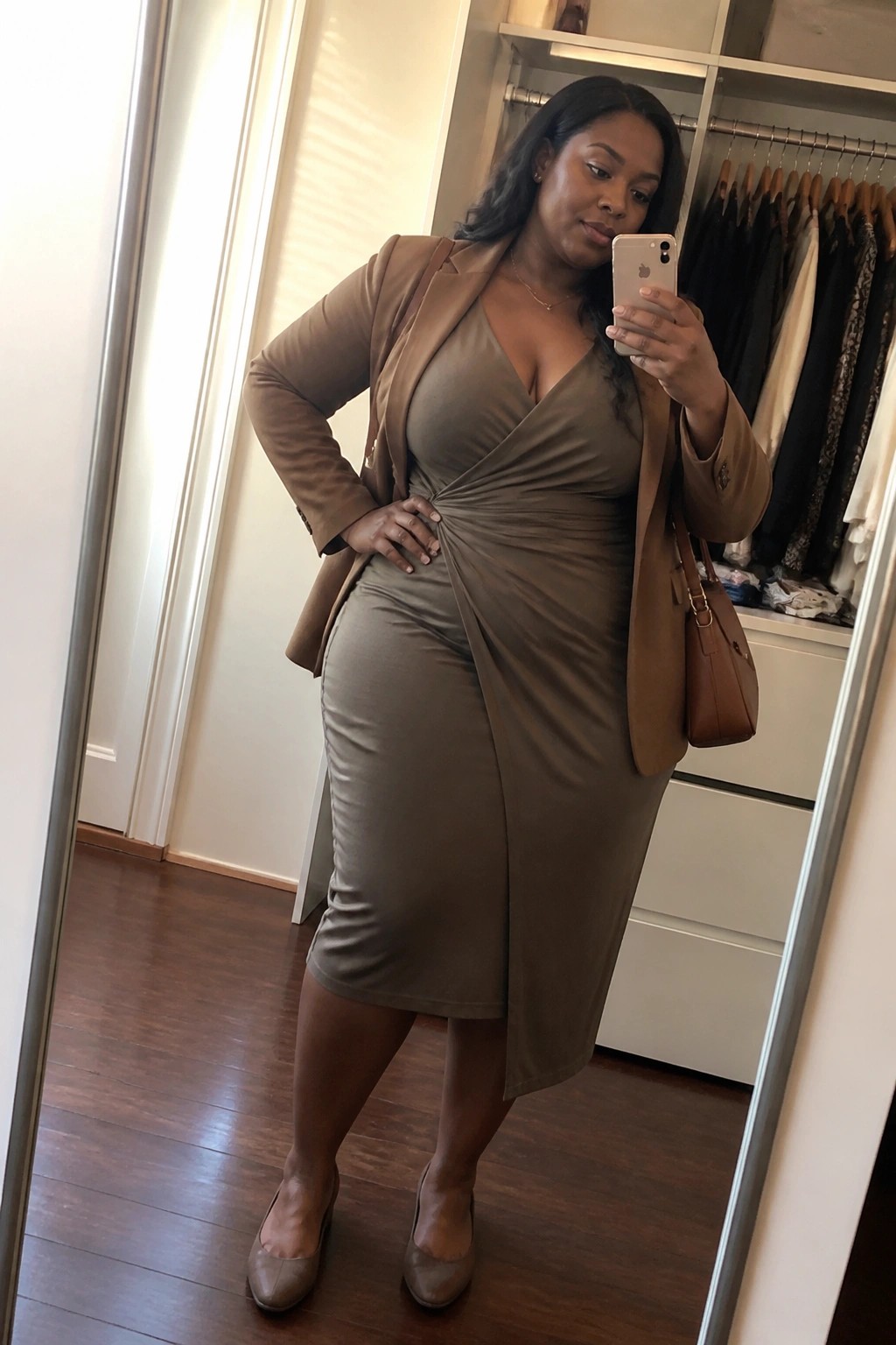 Woman in olive dress and tan blazer taking mirror selfie in closet
