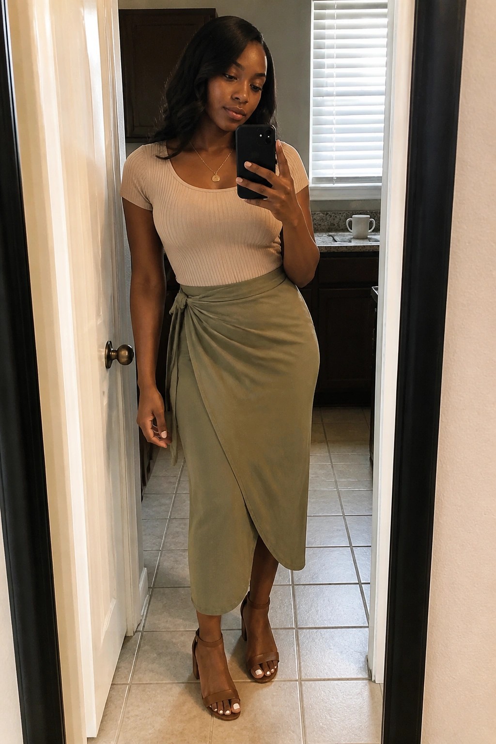Woman wearing a beige ribbed short sleeve top tucked into a sage green wrap midi skirt with a side tie, paired with brown block heel sandals and a delicate gold necklace.