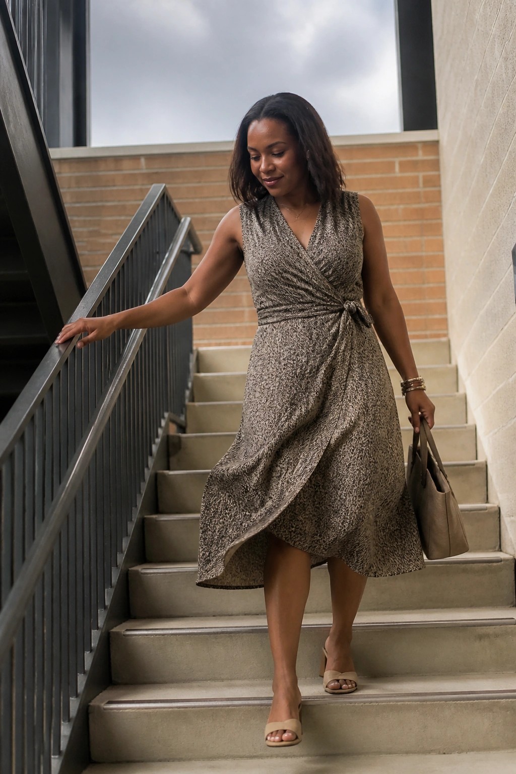 Woman in patterned wrap dress descending stairs holding handbag and wearing heels