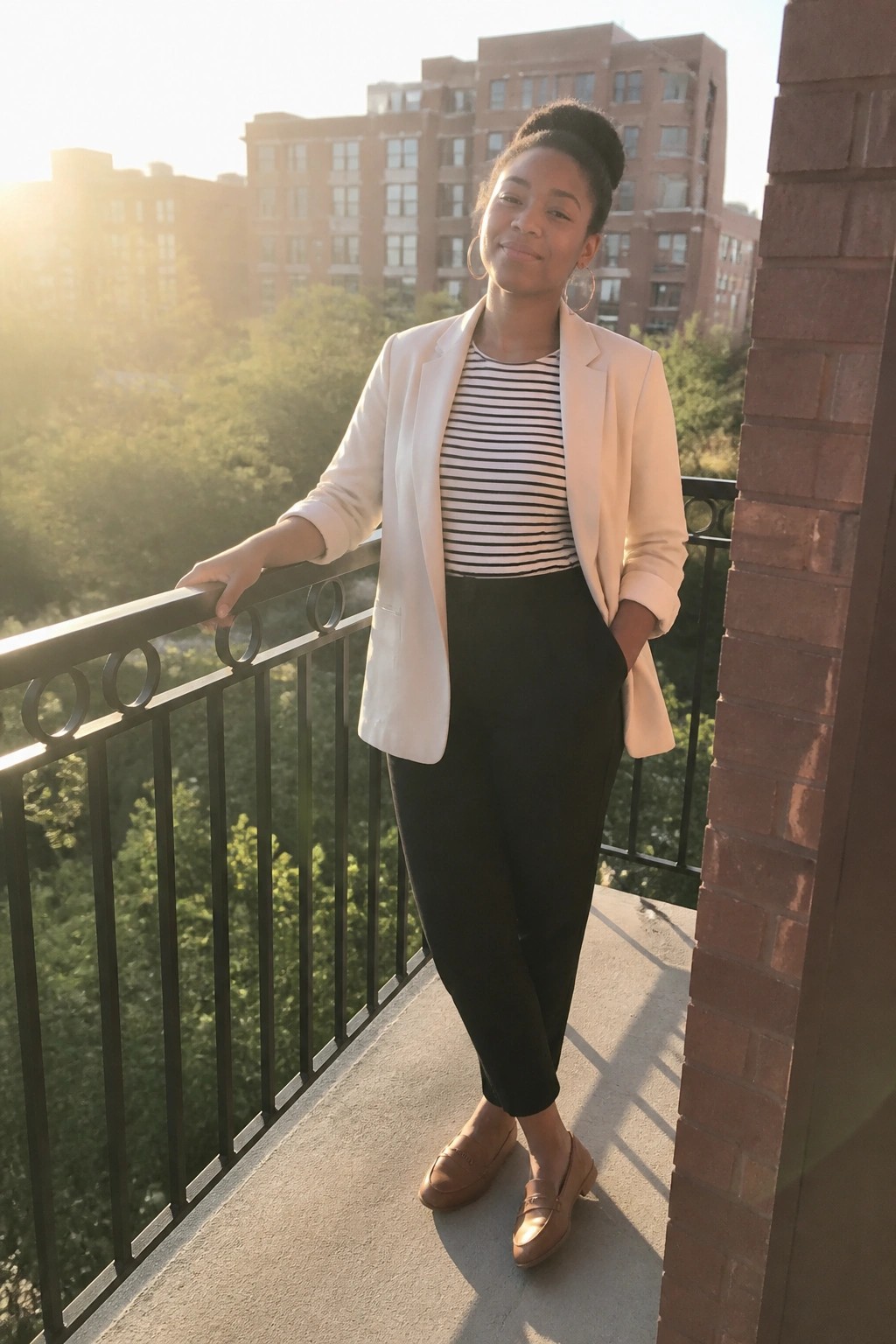 Woman in white blazer and striped shirt on urban balcony at sunset.
