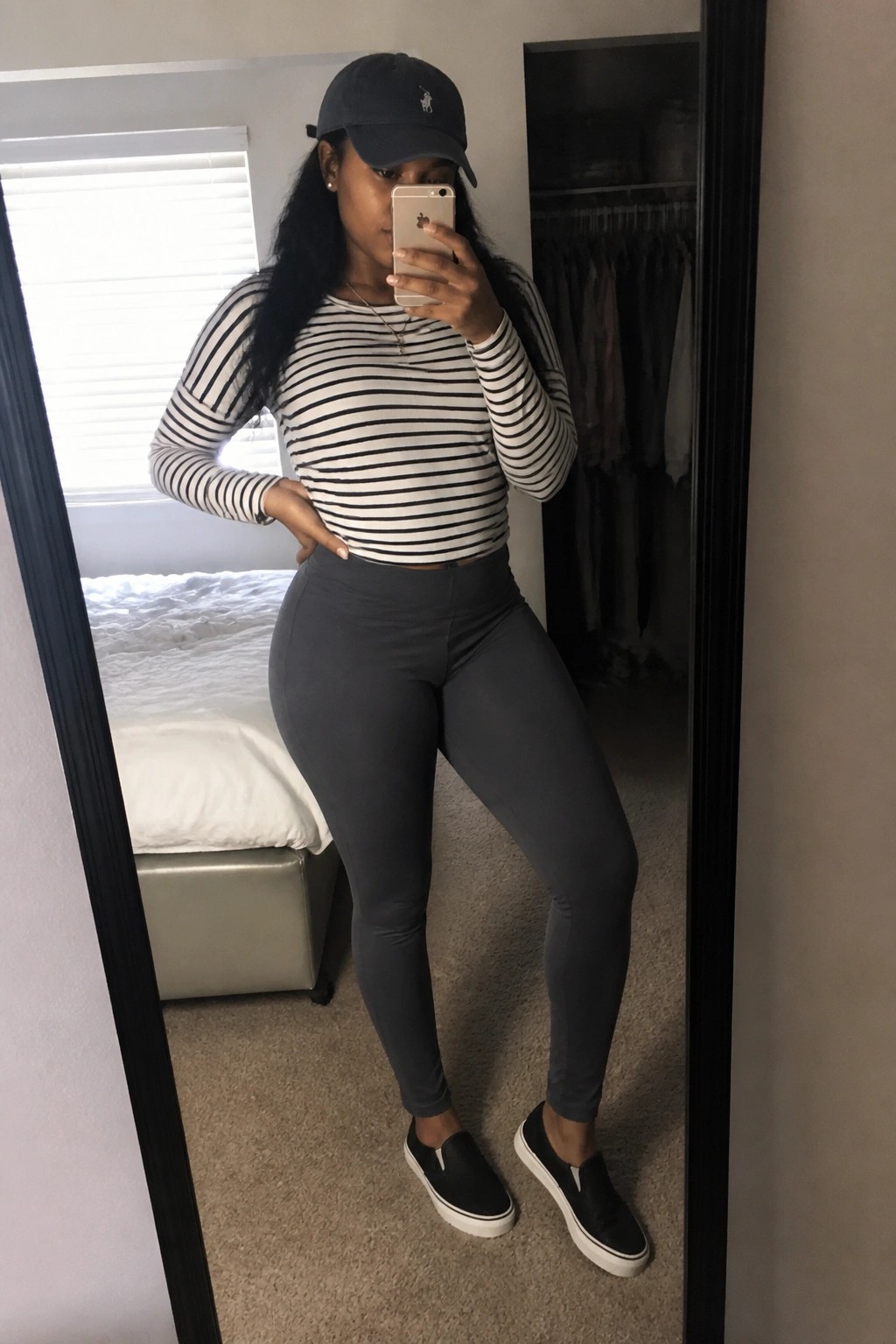 Woman in striped top and gray leggings taking mirror selfie in bedroom
