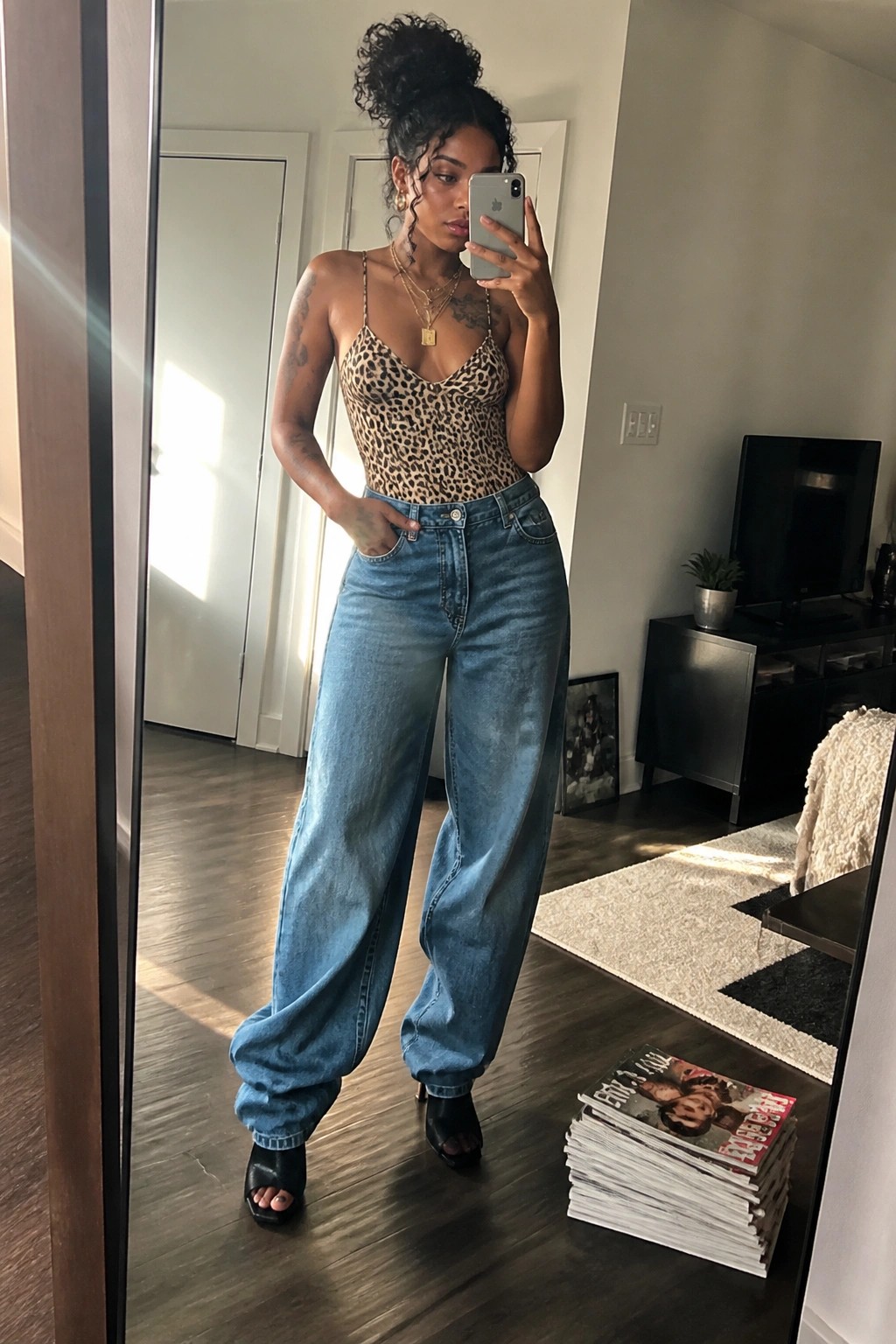 Woman in mirror selfie wearing leopard print bodysuit tucked into baggy blue jeans with black open toe heels and layered gold necklaces.