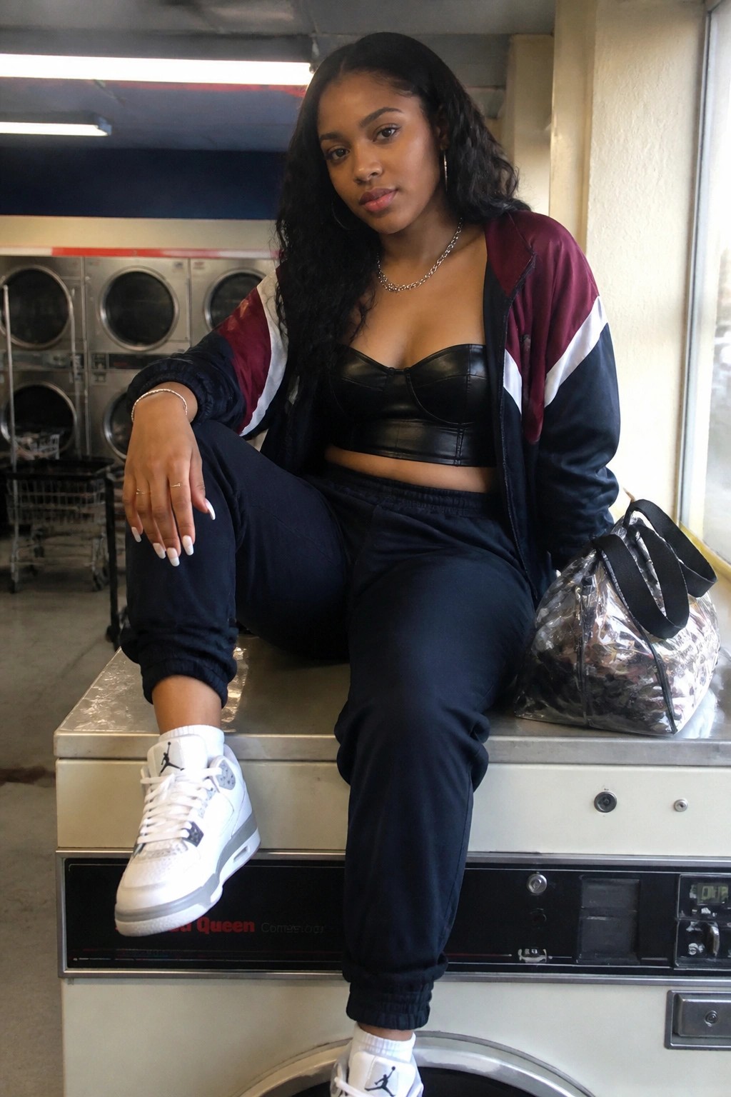 Woman in colorblock track jacket and leather top on laundromat washing machine with bag