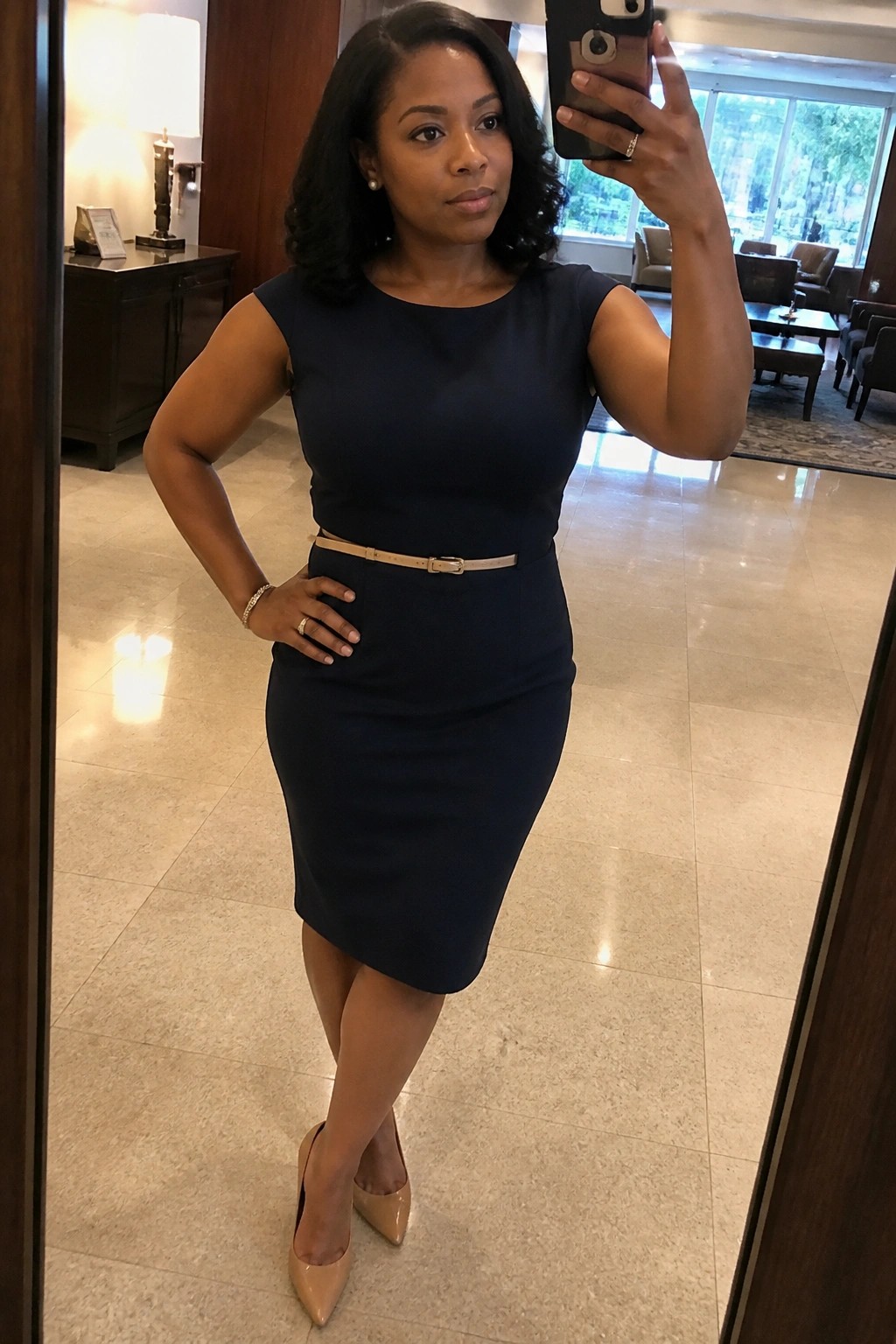 Woman in navy blue dress taking mirror selfie in elegant lobby