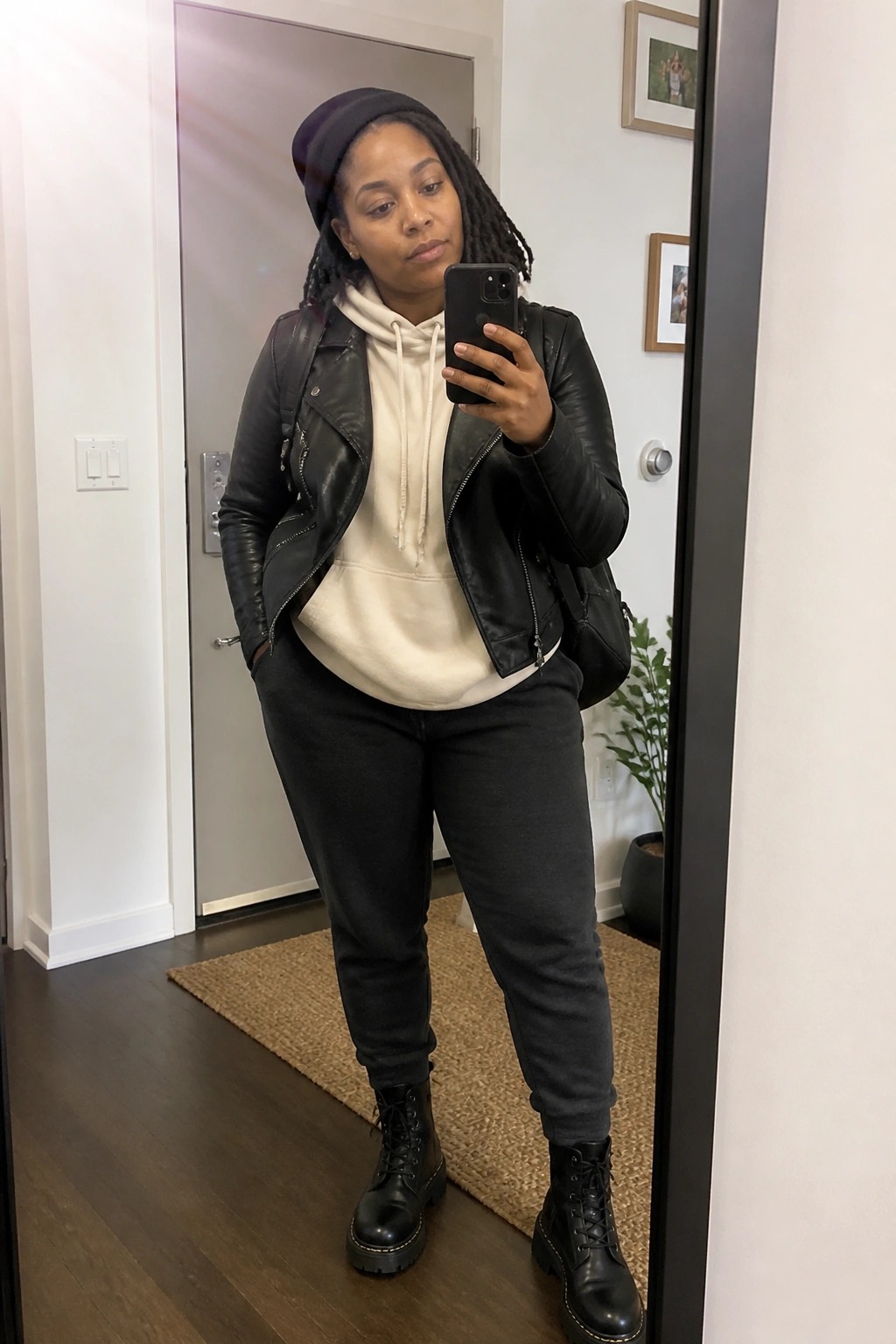Woman in black leather jacket and beanie taking mirror selfie with phone