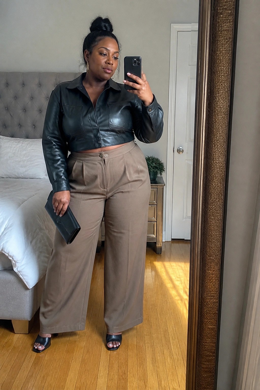 Woman in cropped black leather jacket and wide brown pants taking mirror selfie