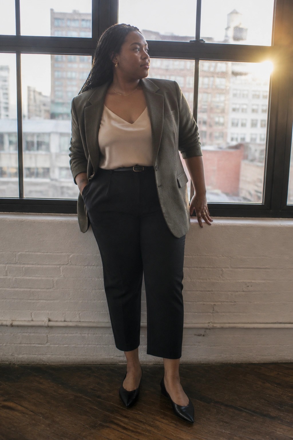 Woman in olive blazer and black pants by sunlit city window
