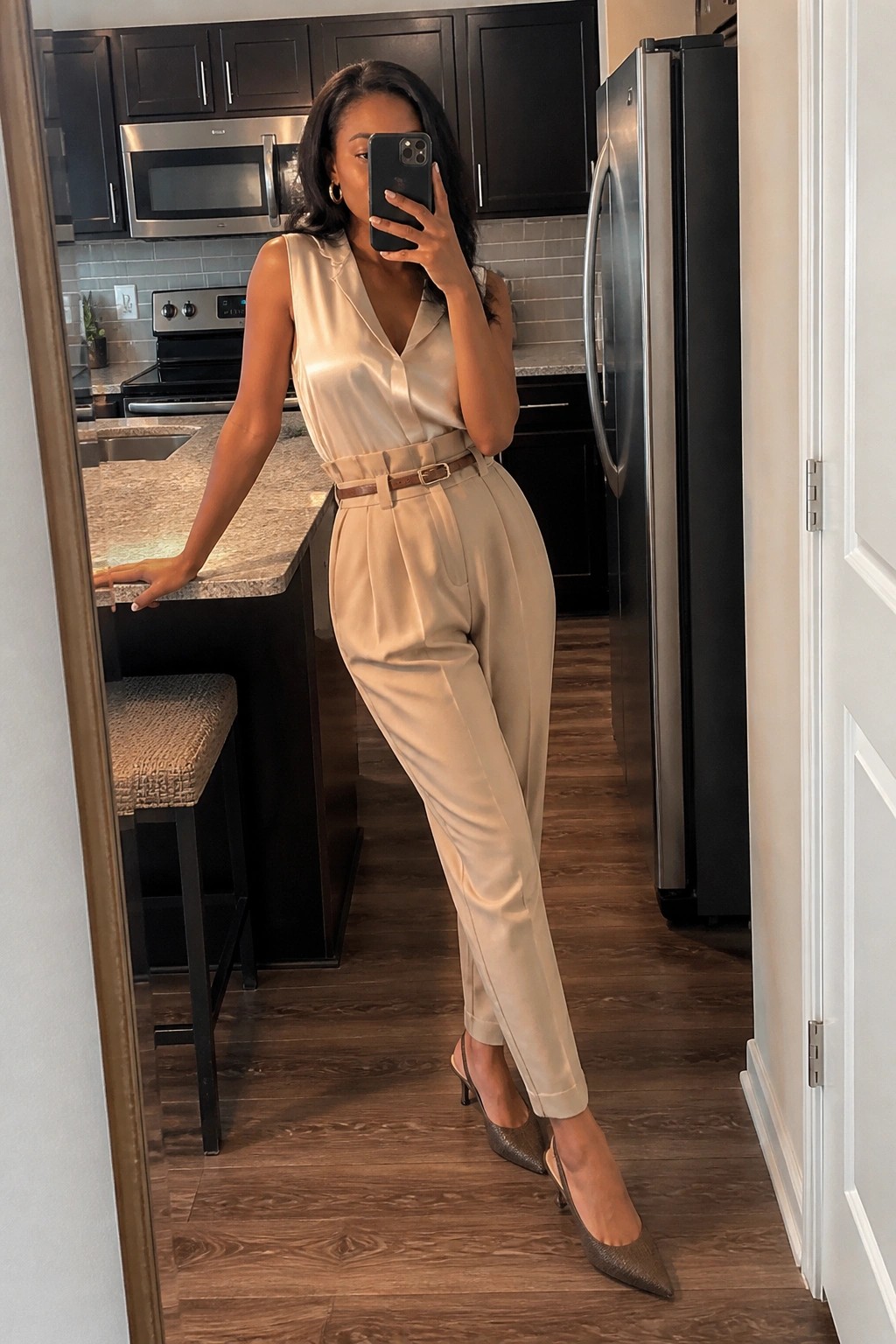 Woman in beige satin top and pants taking mirror selfie in kitchen