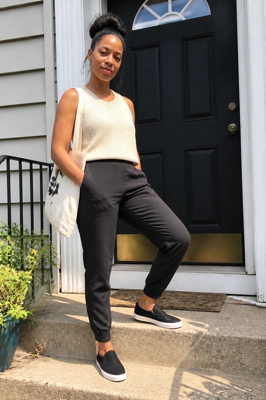Woman in cream knit top and black joggers with tote bag at doorway
