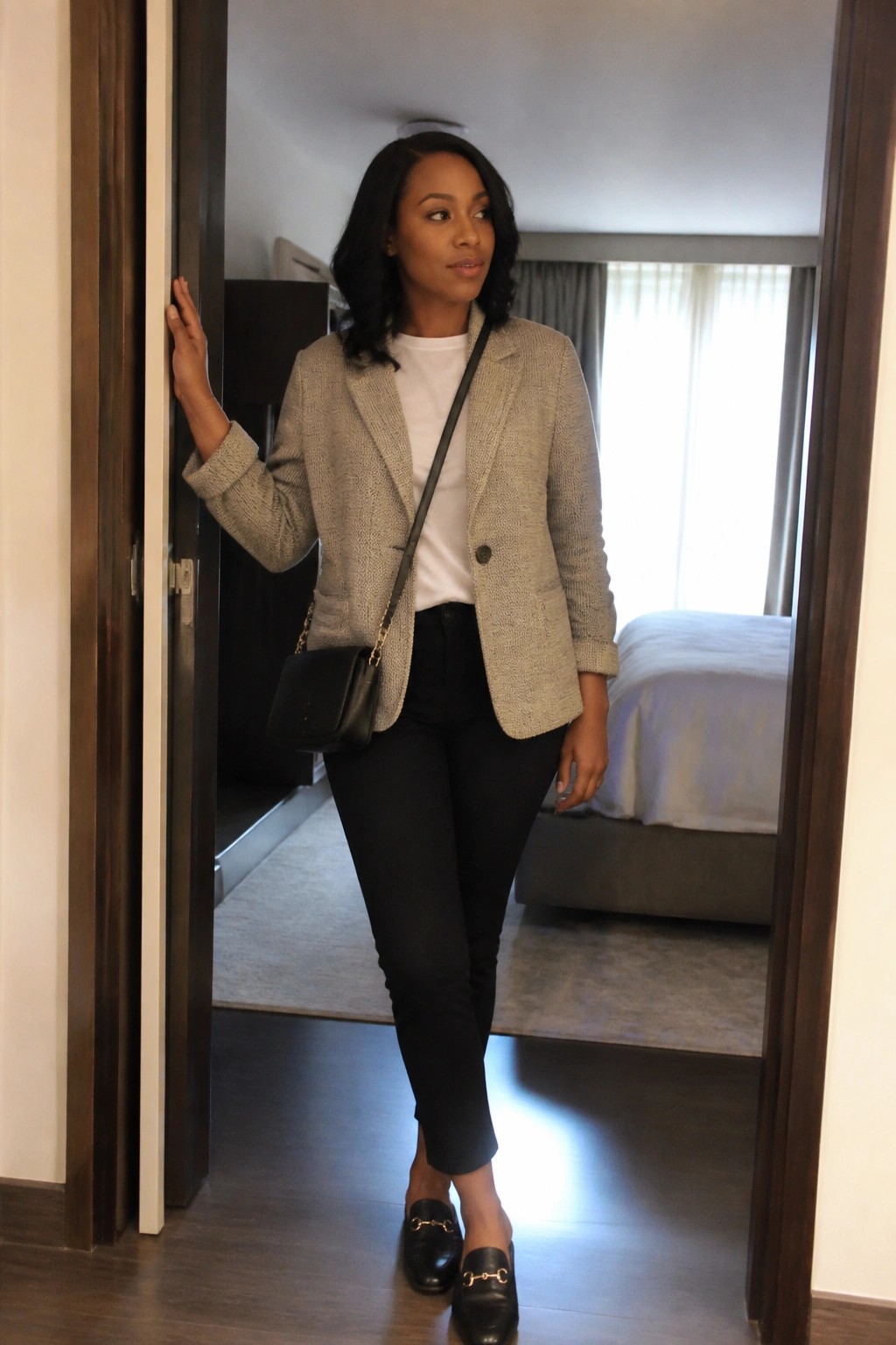 Woman in beige blazer and black pants leaning in bedroom doorway