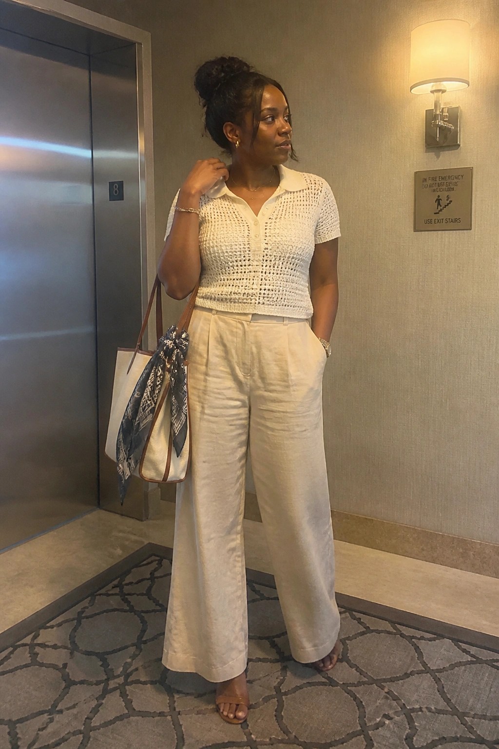 Woman in white crocheted polo shirt and wide-leg pants carrying a tote bag