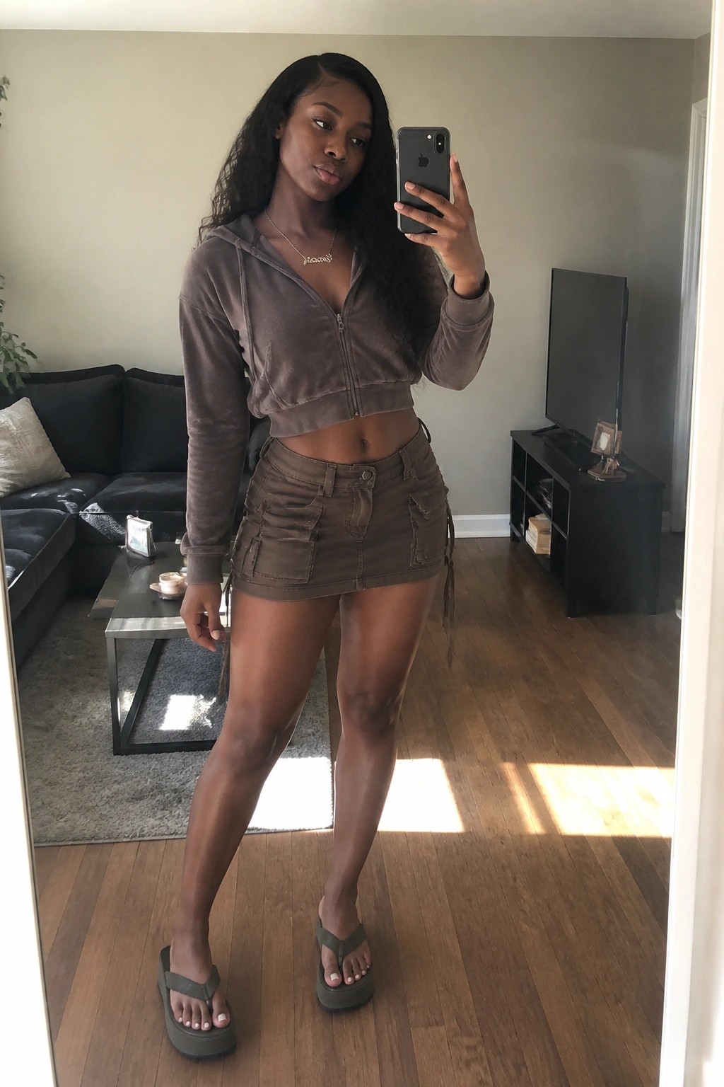 Woman in brown velour cropped hoodie and cargo skirt taking mirror selfie