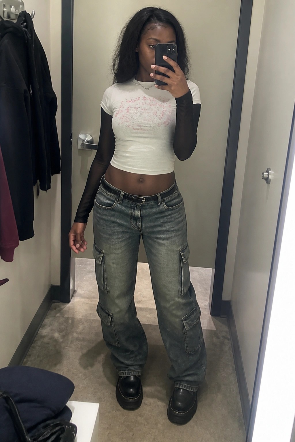 Woman in white crop top and baggy cargo jeans taking mirror selfie in fitting room
