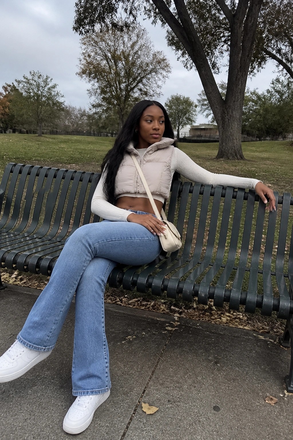 Young Black woman in beige puffer vest and jeans on park bench