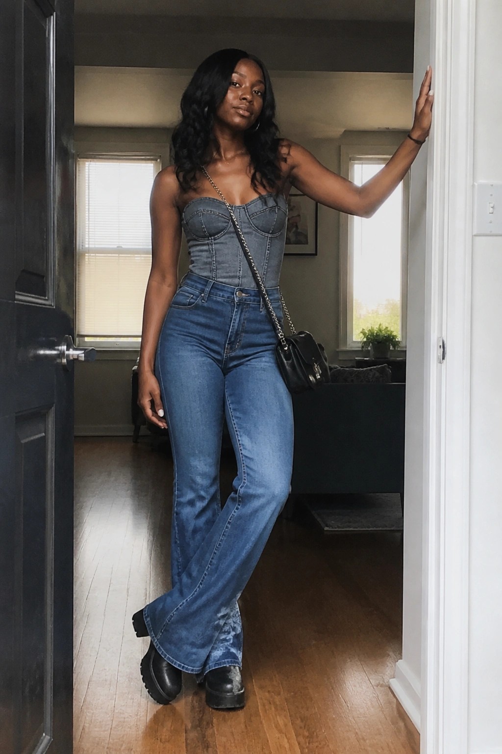 Woman in denim corset top and flared jeans posing in doorway with bag