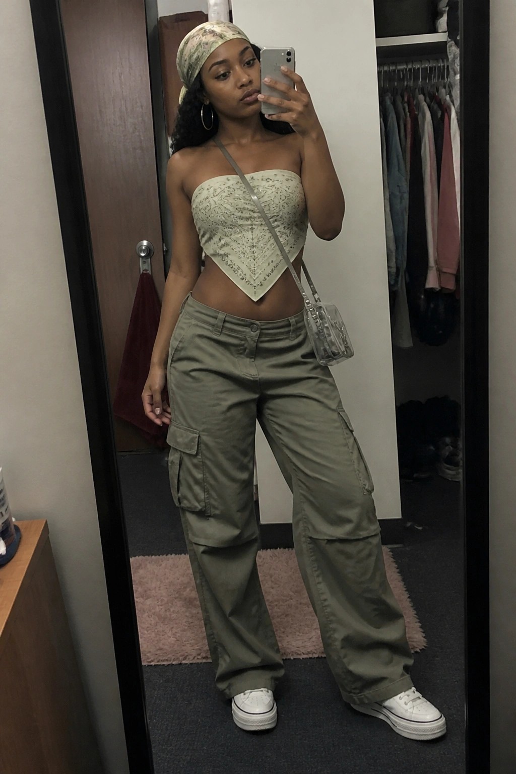 Woman in floral headscarf, sage bandeau top, and olive cargo pants taking mirror selfie.