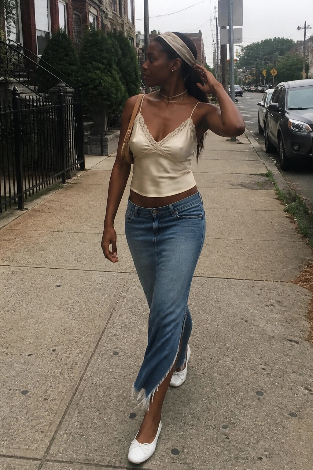 Woman in cream satin camisole and frayed jeans walking on city sidewalk.