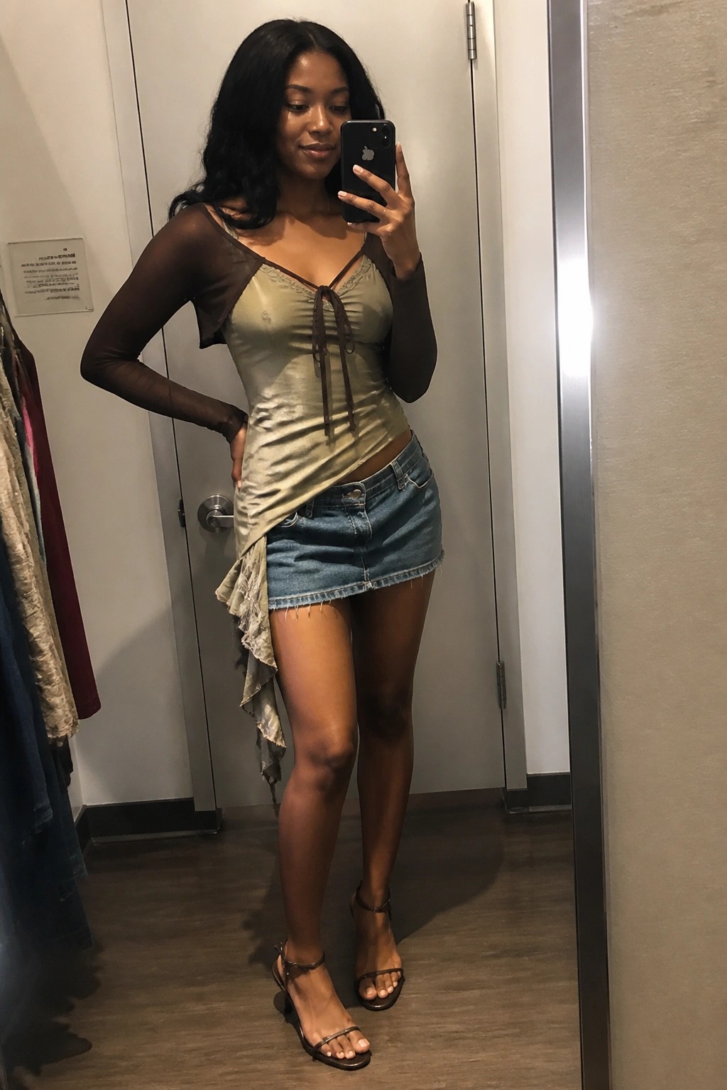 Woman in green satin top and denim skirt taking mirror selfie with phone