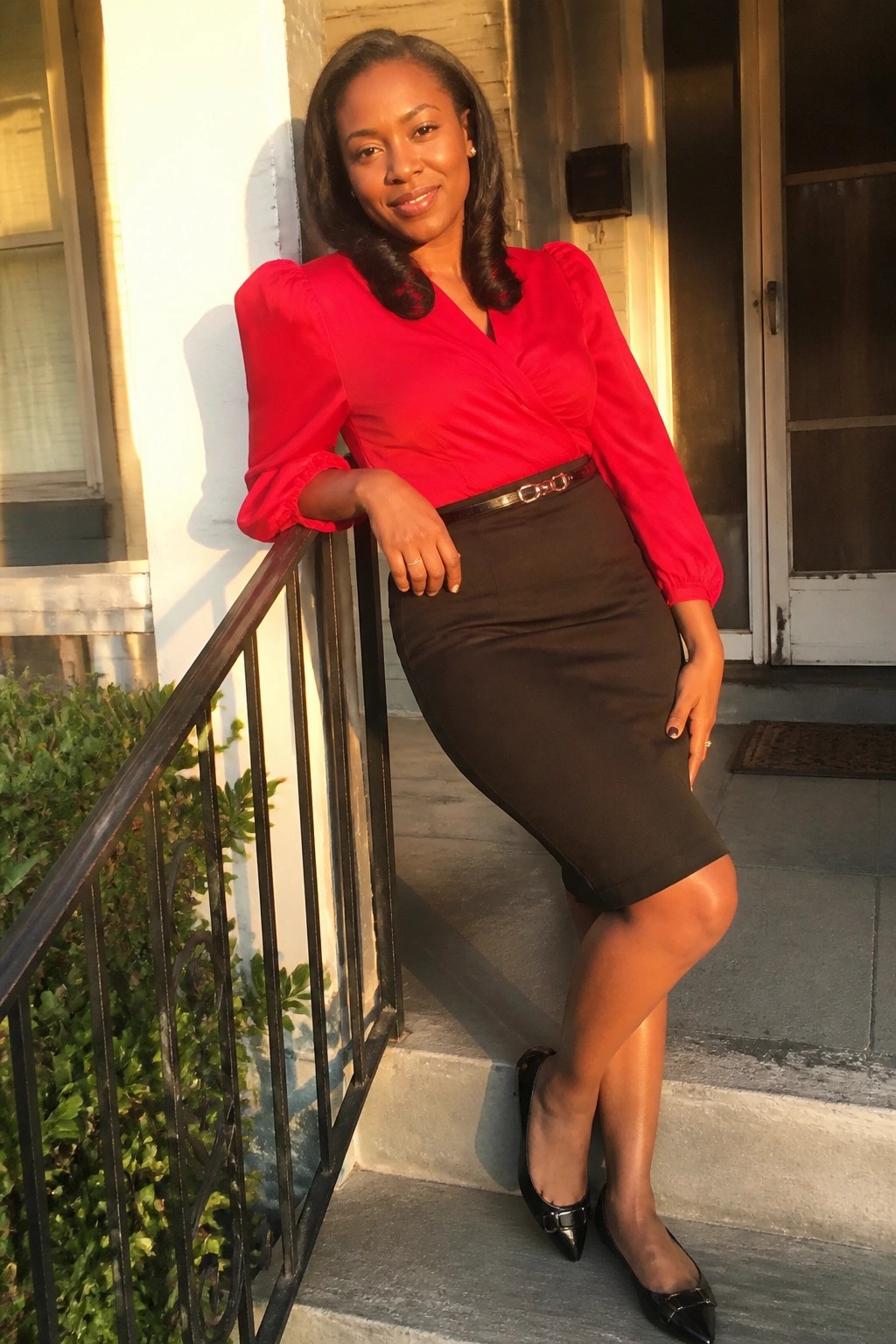 Woman in red blouse and brown skirt posing on building steps at sunset