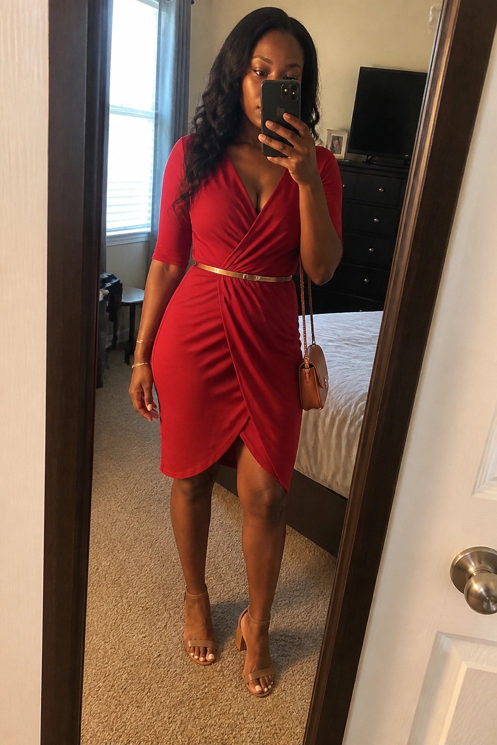 Woman in red wrap dress taking mirror selfie in bedroom with gold belt