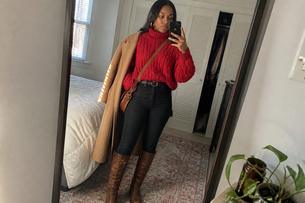 18 Cozy Red Winter Outfits for Black Women Using Layers, Boots, and Rich Textures Woman in red turtleneck sweater, black jeans, and brown boots taking mirror selfie