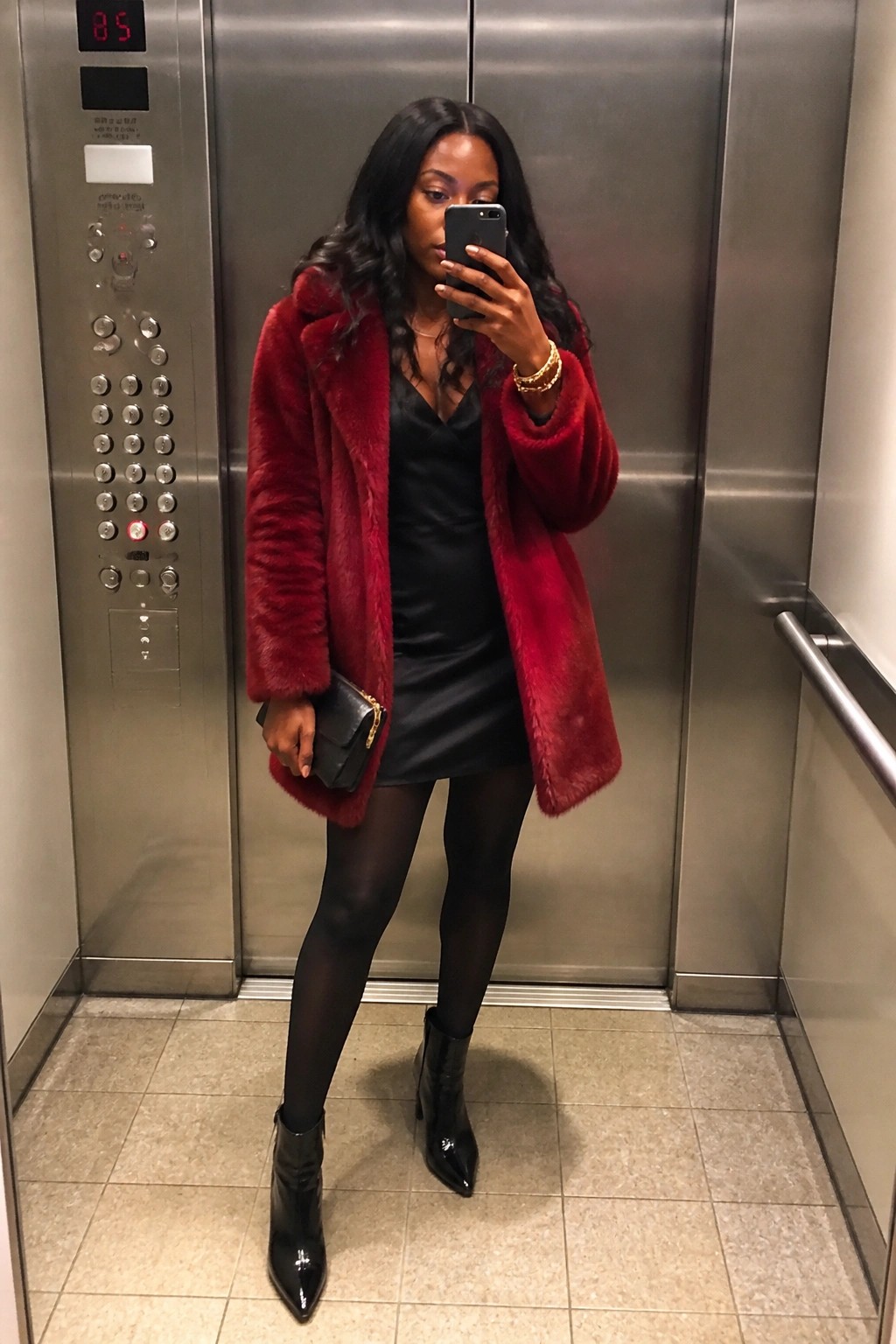 Woman in red fur coat over black dress taking selfie in elevator