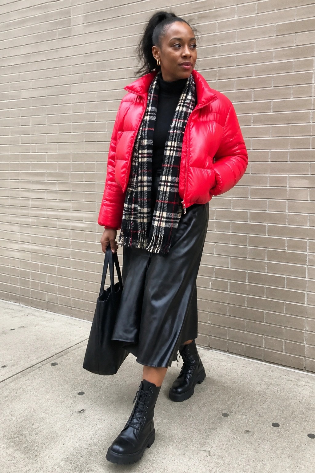 Woman in red puffer jacket, plaid scarf, black leather skirt, and combat boots