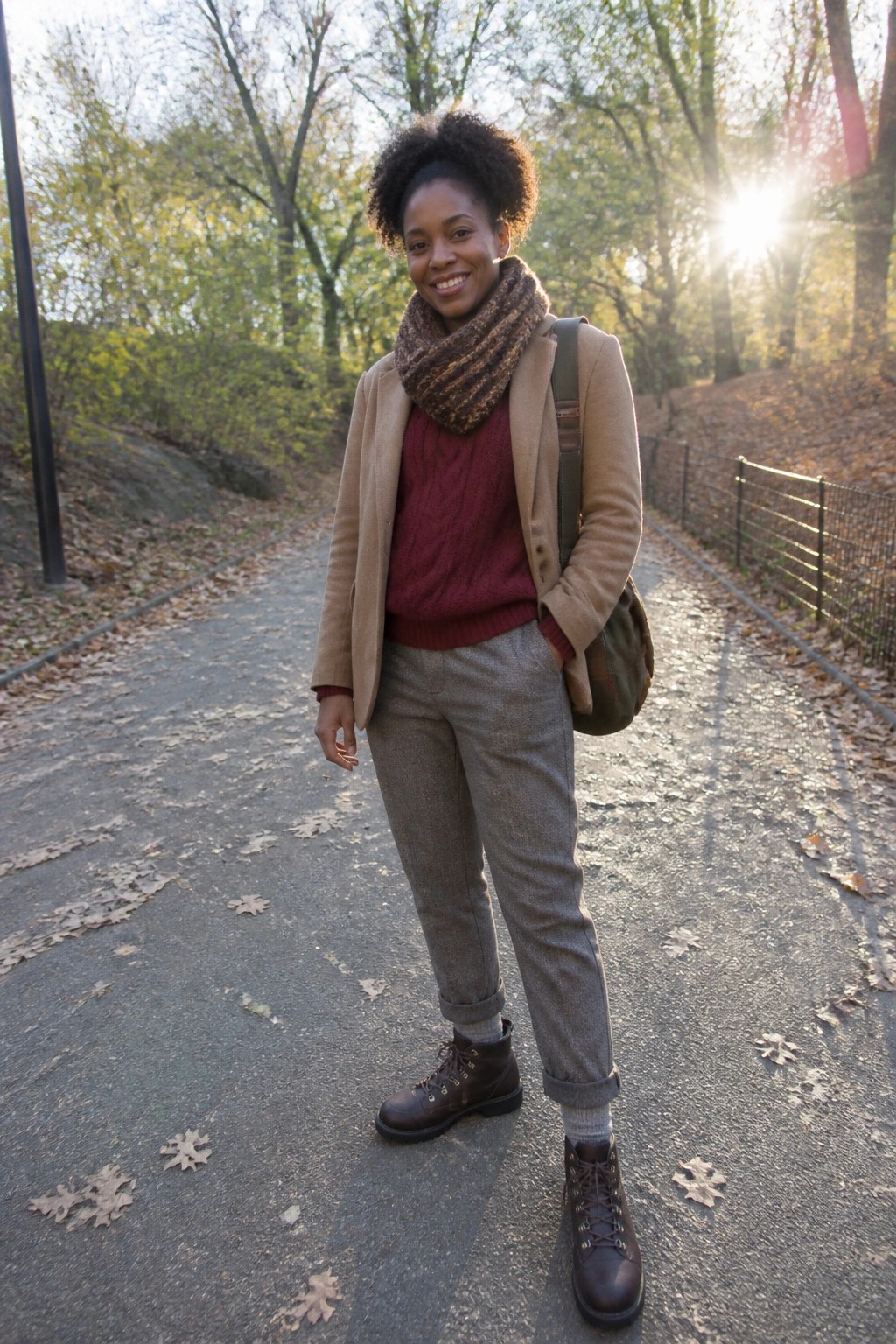Smiling woman in red sweater, tan coat, and scarf on sunny autumn path