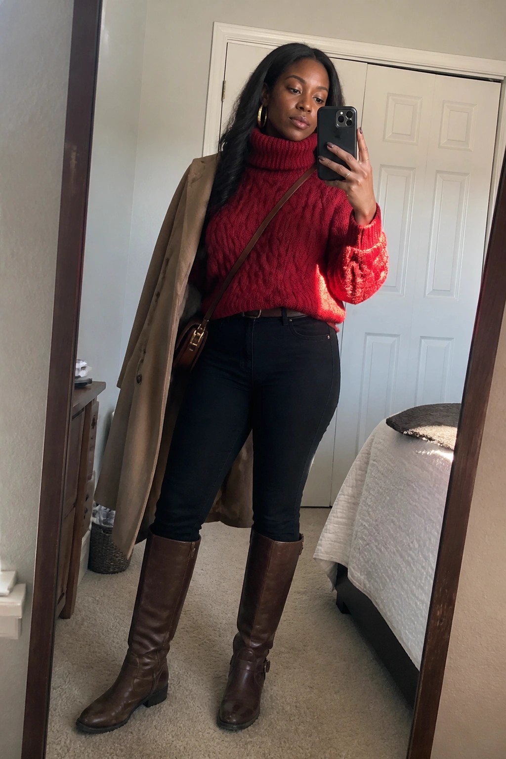 Woman in red turtleneck sweater, black jeans, and brown boots taking mirror selfie