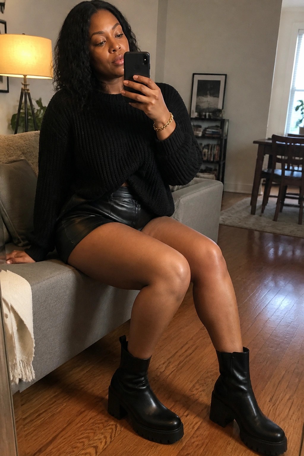Woman in black sweater and leather skirt taking selfie on gray couch