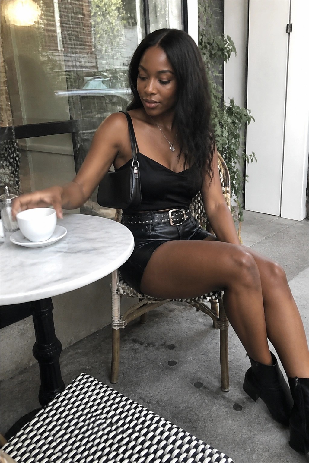 Woman in black satin top and leather skirt reaches for coffee at outdoor cafe