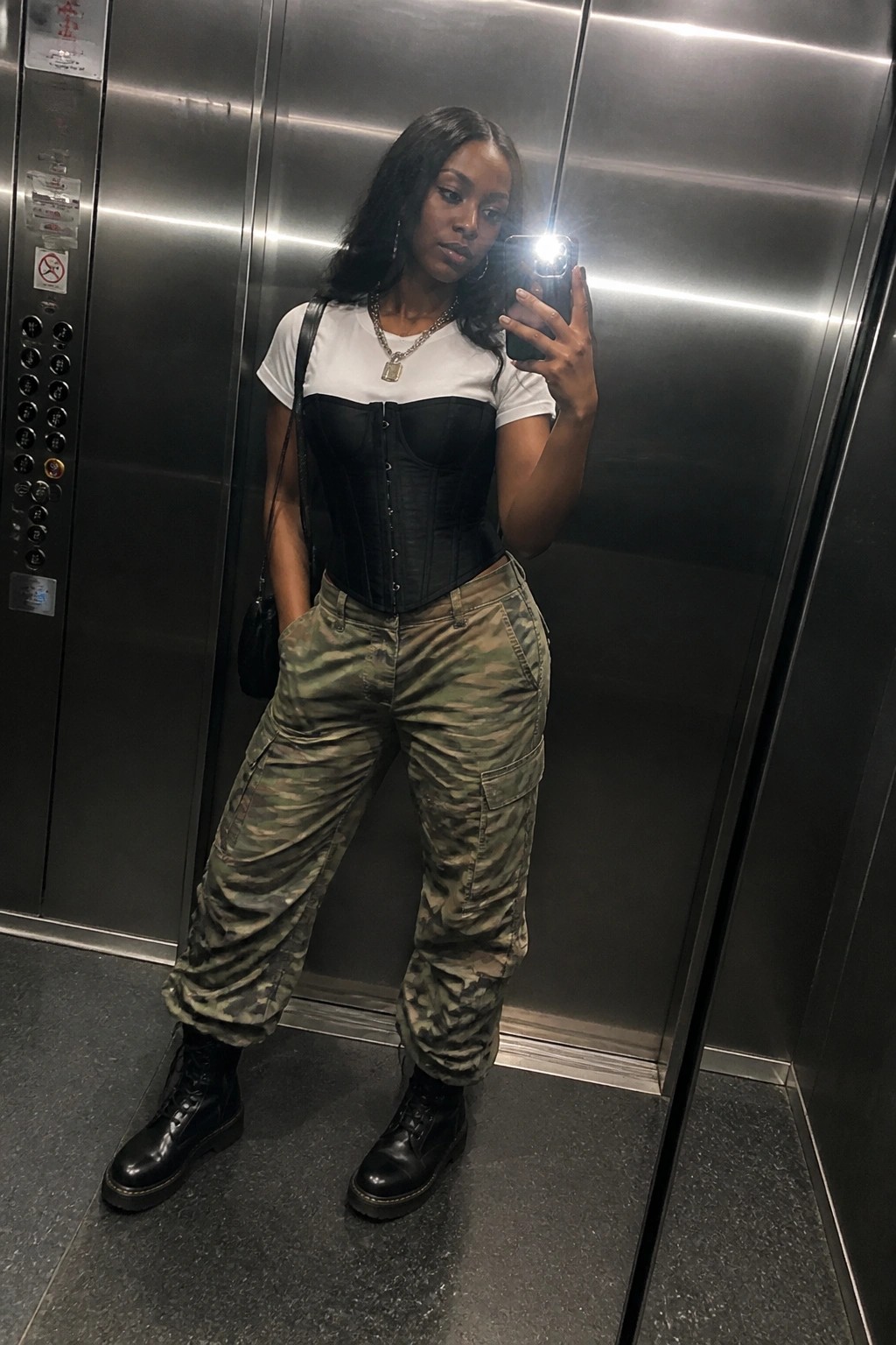 Woman in black corset, camouflage cargo pants, and boots taking elevator selfie