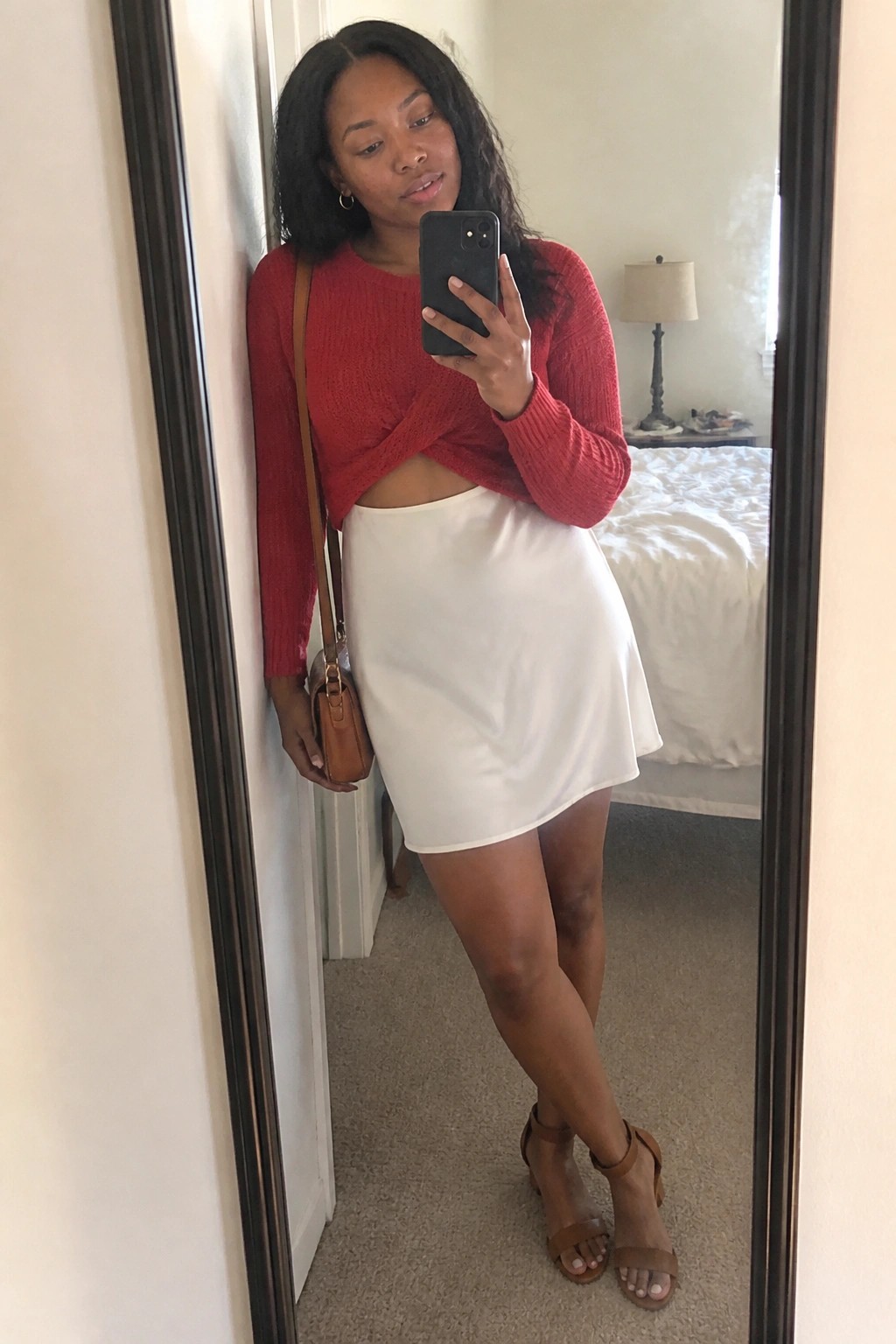 Woman in red twist-front crop sweater and white mini skirt taking mirror selfie