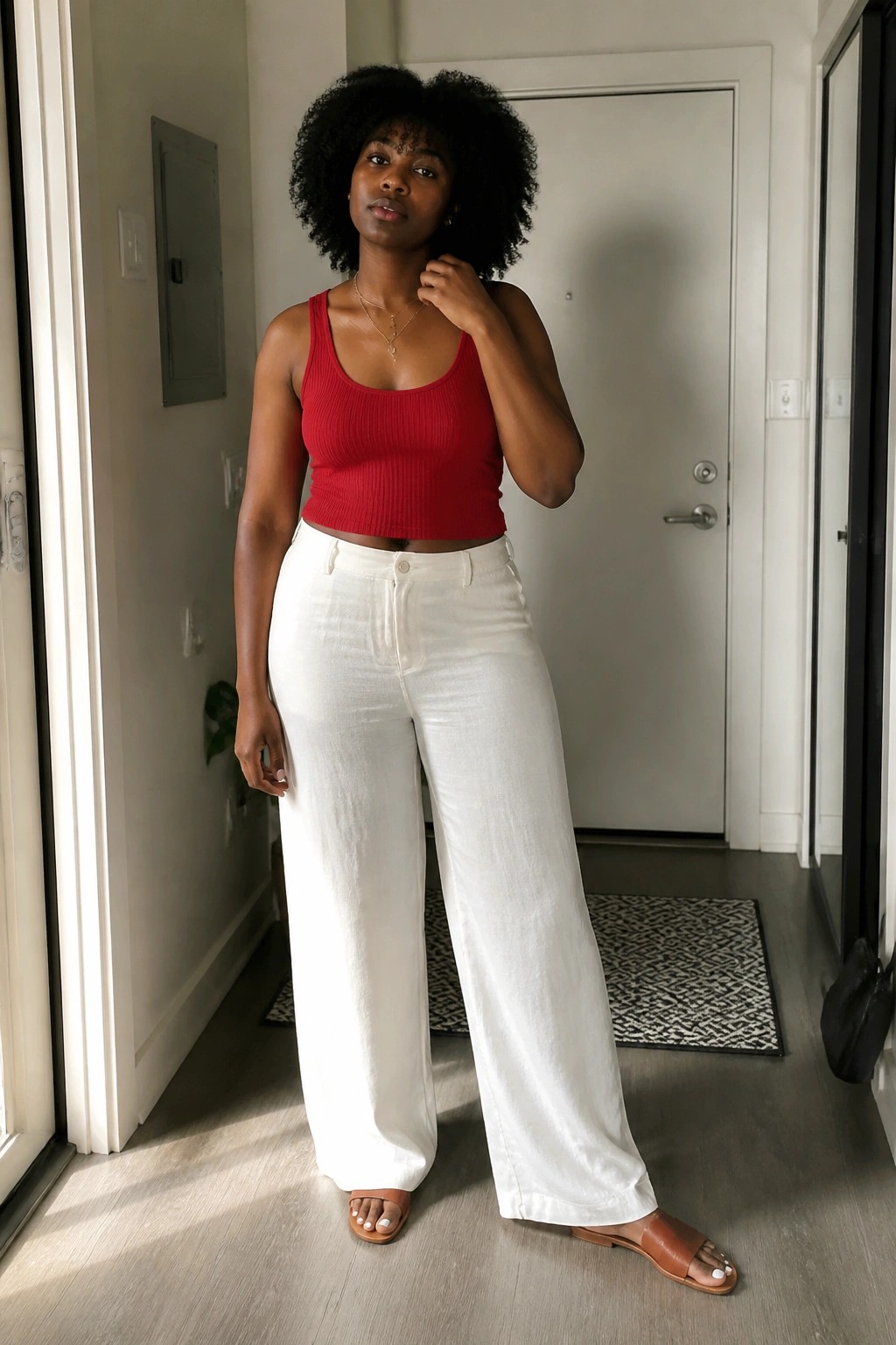 Woman with curly afro hair in red tank top and white wide-leg pants indoors