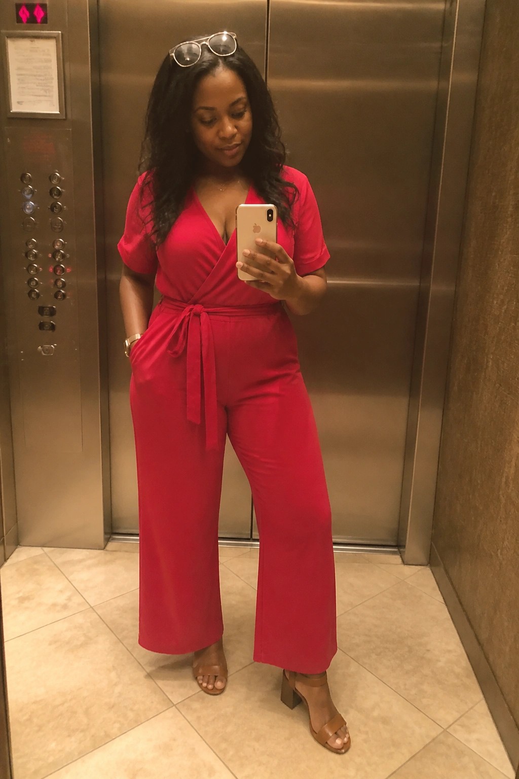 Woman in red jumpsuit taking mirror selfie in elevator with gold iPhone