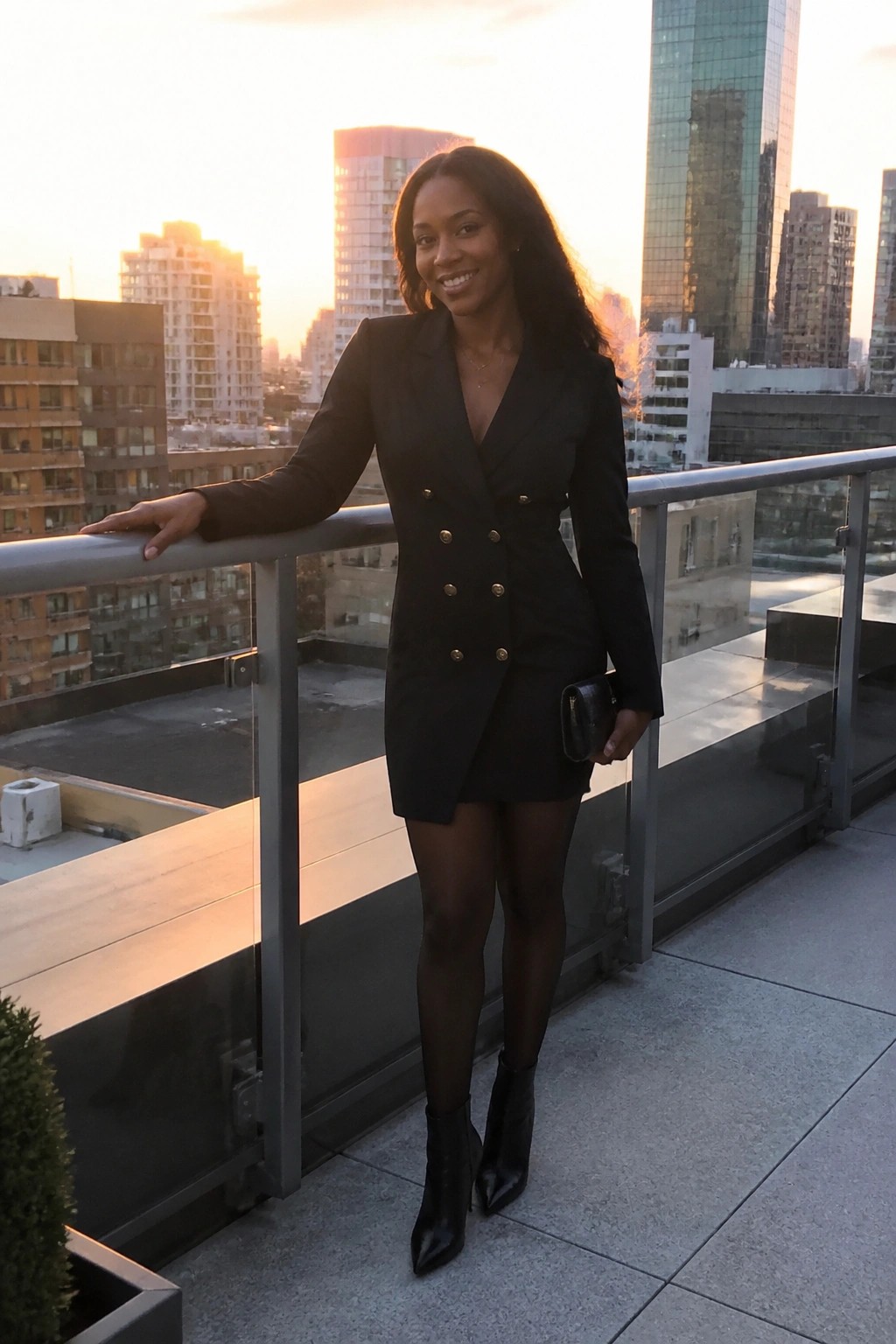 Woman in black double-breasted blazer dress on city rooftop at sunset