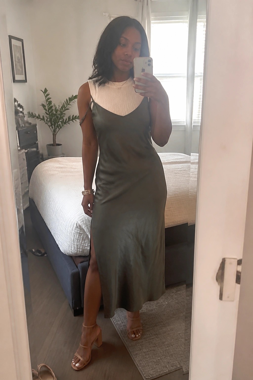 Woman in olive-green satin slip dress taking mirror selfie in bedroom