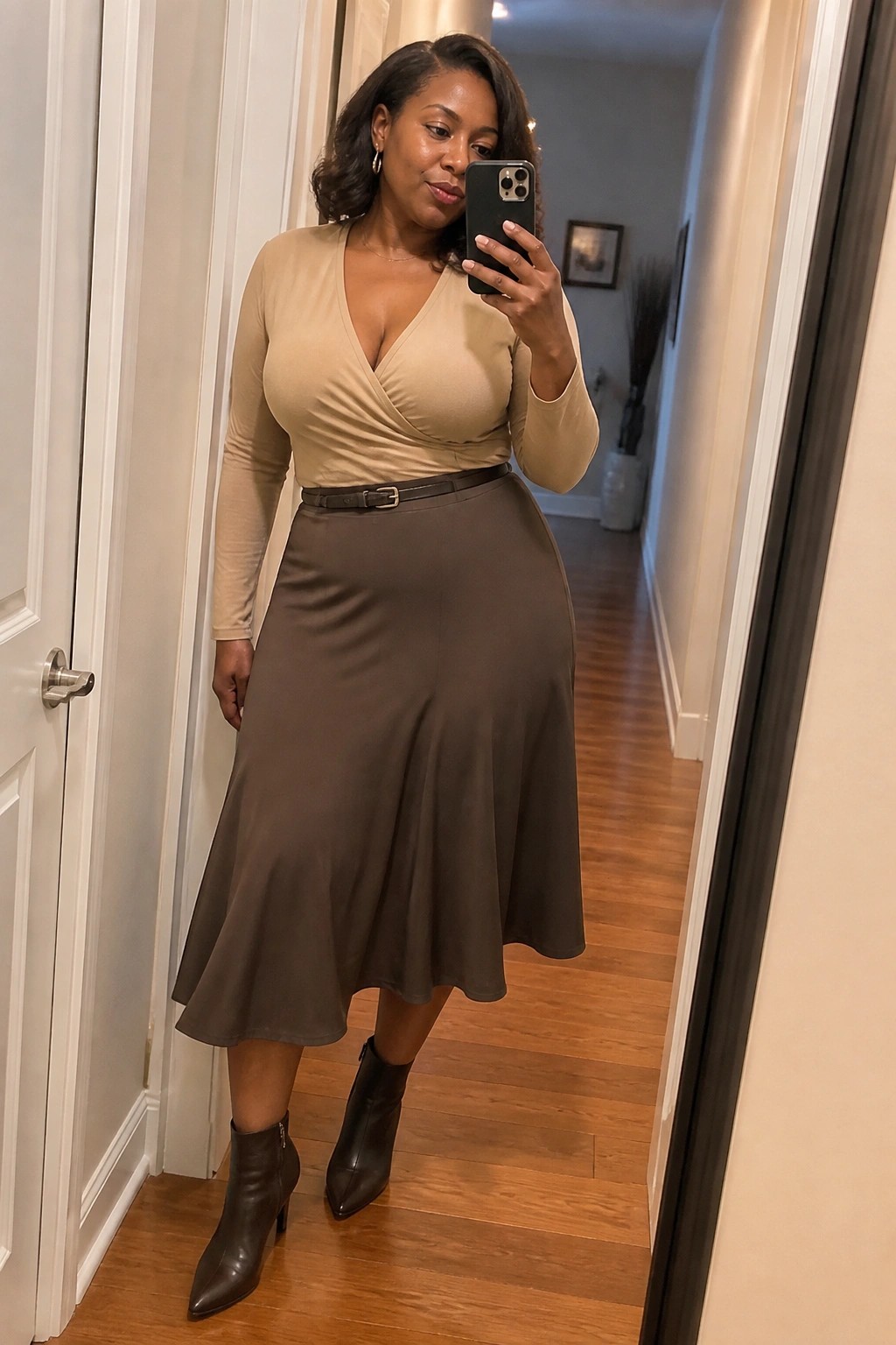 Woman in beige top and brown skirt taking mirror selfie in hallway