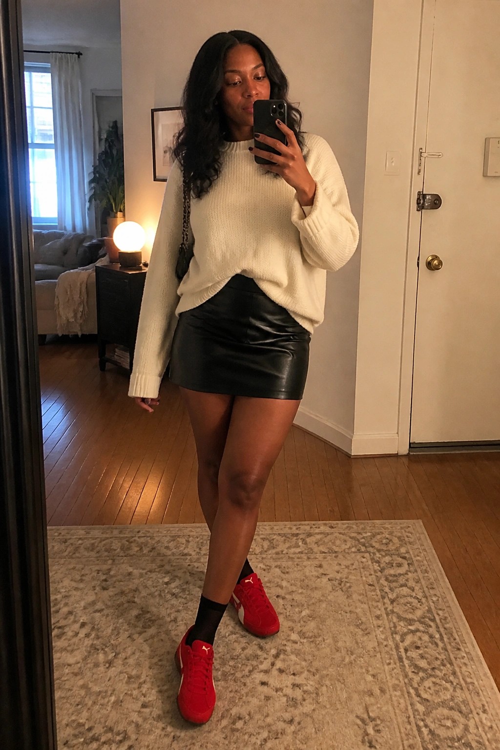 Woman in white knit sweater and black leather skirt with red sneakers taking mirror selfie