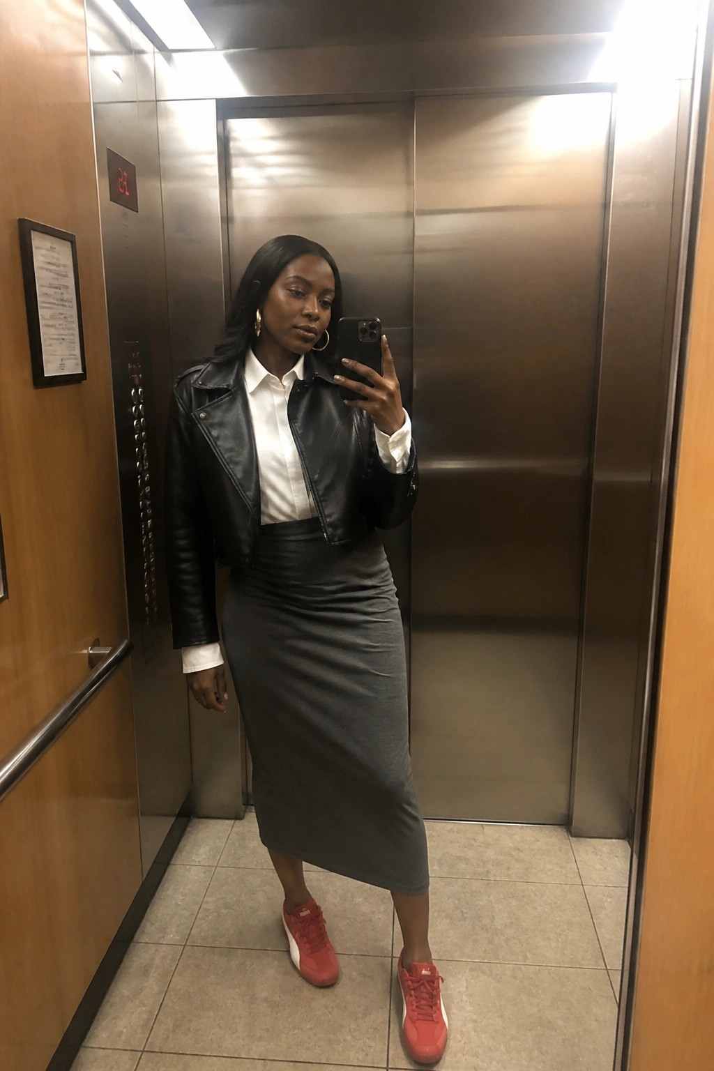 Woman in black leather jacket and gray skirt takes mirror selfie in elevator
