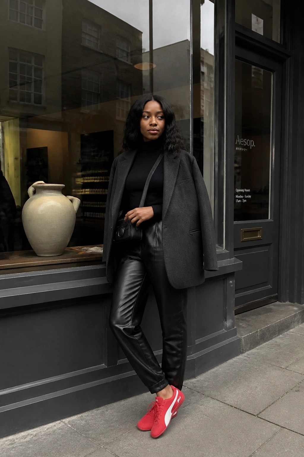 Woman in black leather pants, gray blazer, and red sneakers outside Aesop store