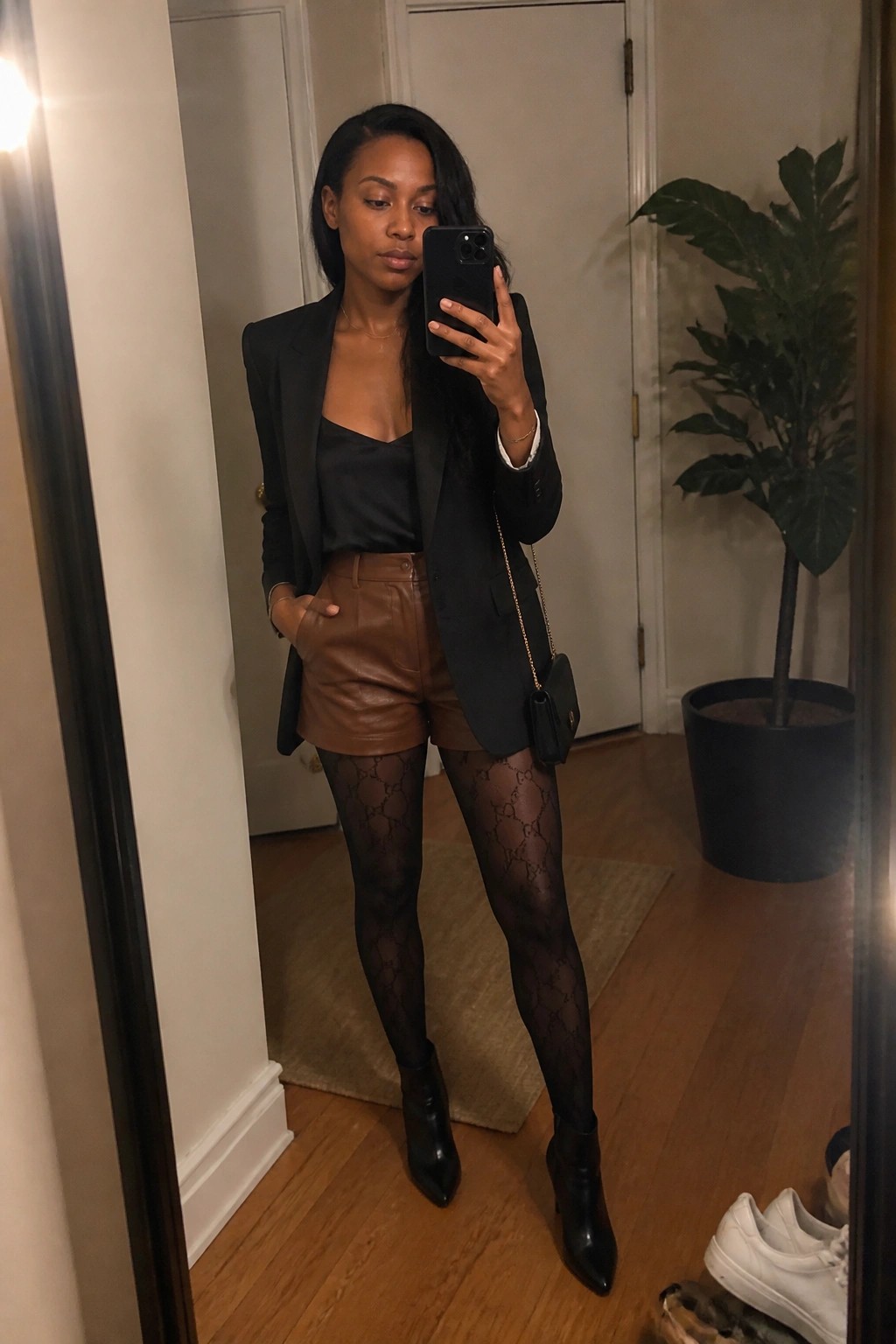 Woman in black blazer and brown shorts taking mirror selfie with phone.