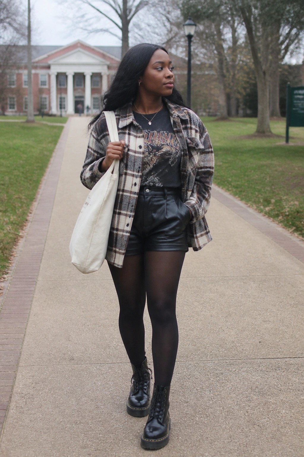 Woman in plaid flannel over graphic tee, leather shorts, and boots on campus path