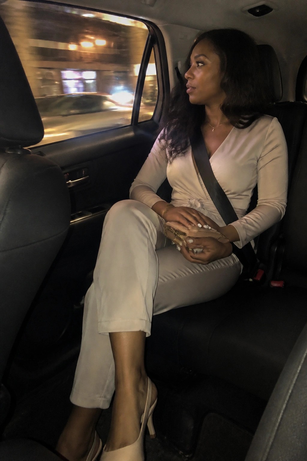 Woman in beige outfit with seatbelt in moving car at night