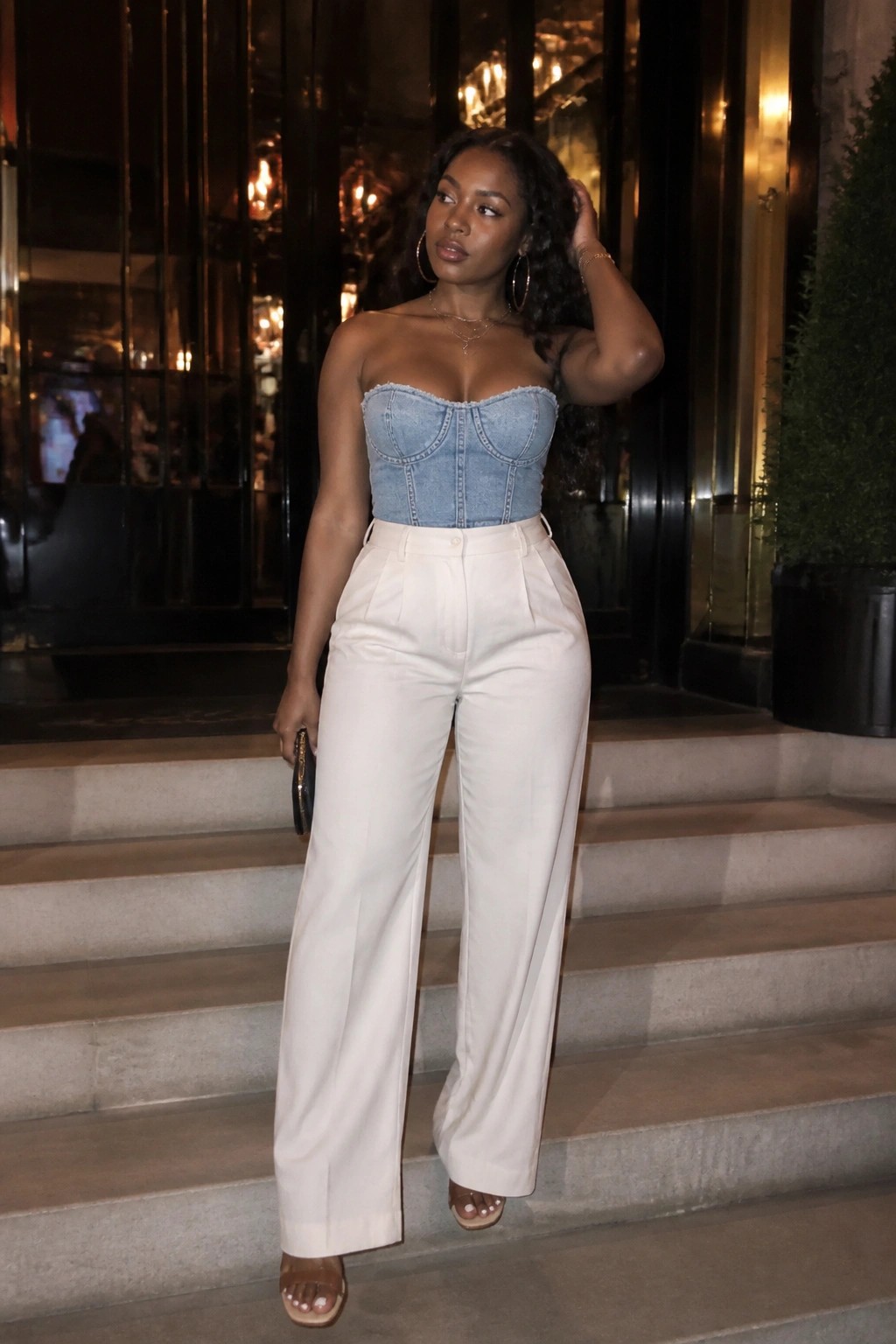 Woman in strapless denim top and white wide-leg pants on nighttime steps