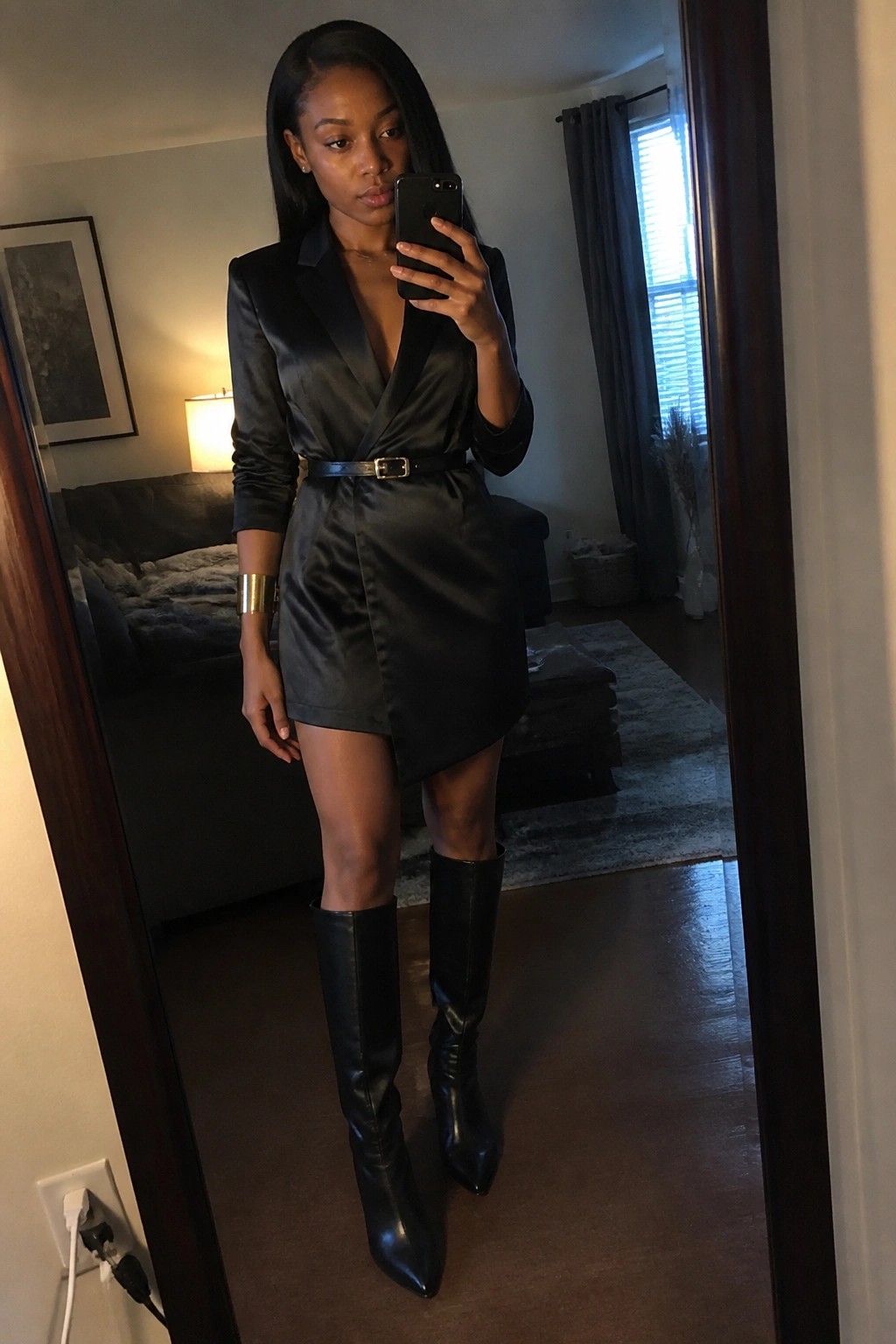 Woman in black satin blazer dress and knee-high boots taking mirror selfie