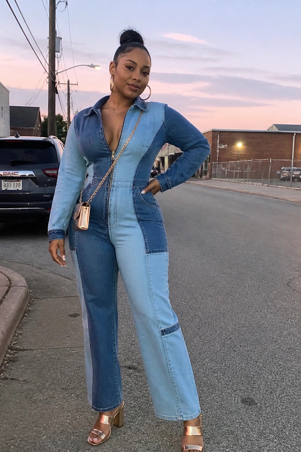 Woman in two-tone denim jumpsuit with gold chain bag posing on street at dusk