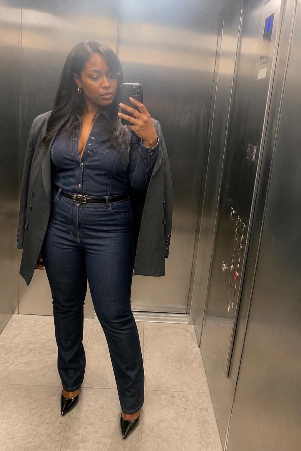 Woman in denim shirt and jeans with blazer taking elevator selfie