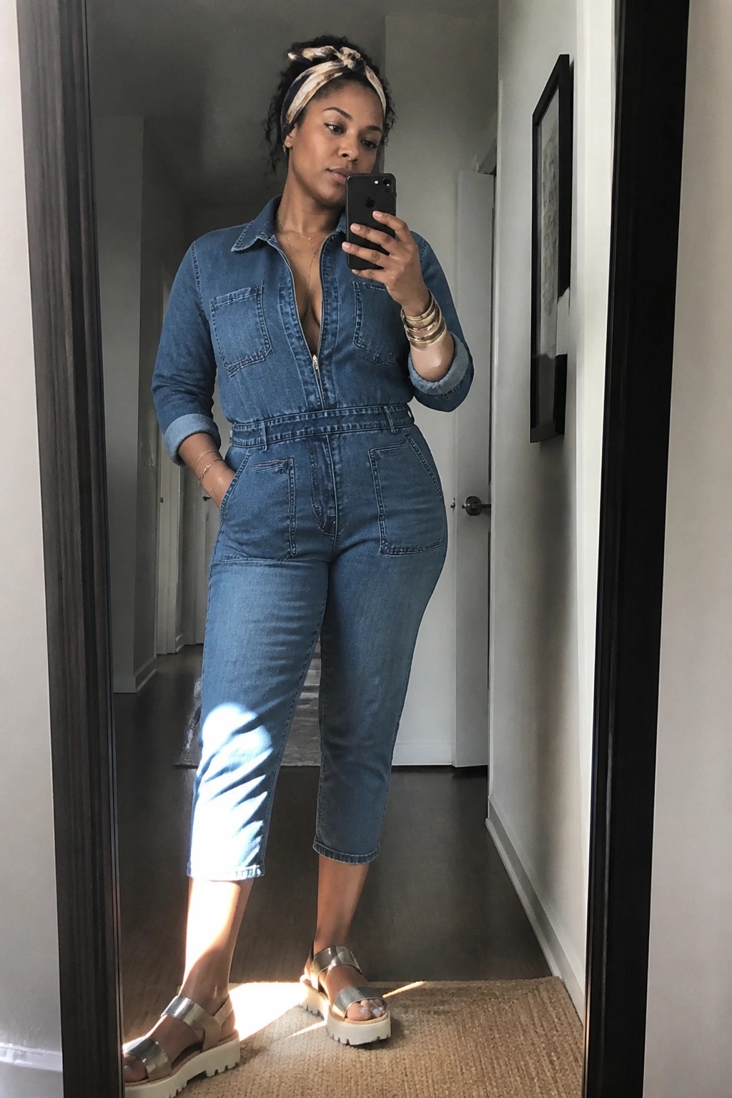 Woman in blue denim jumpsuit taking mirror selfie wearing silver platform sandals